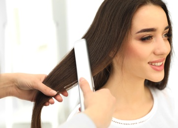 Photo of Hairdresser using modern flat iron to style client's hair in salon