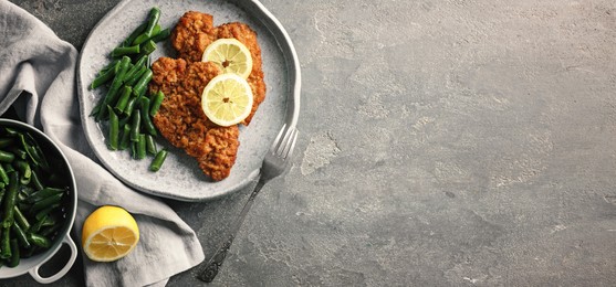 Image of Tasty schnitzels served with lemon and green beans on grey table, flat lay. Banner design with space for text
