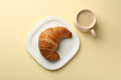 Photo of Delicious fresh croissant and cup of coffee on beige table, flat lay