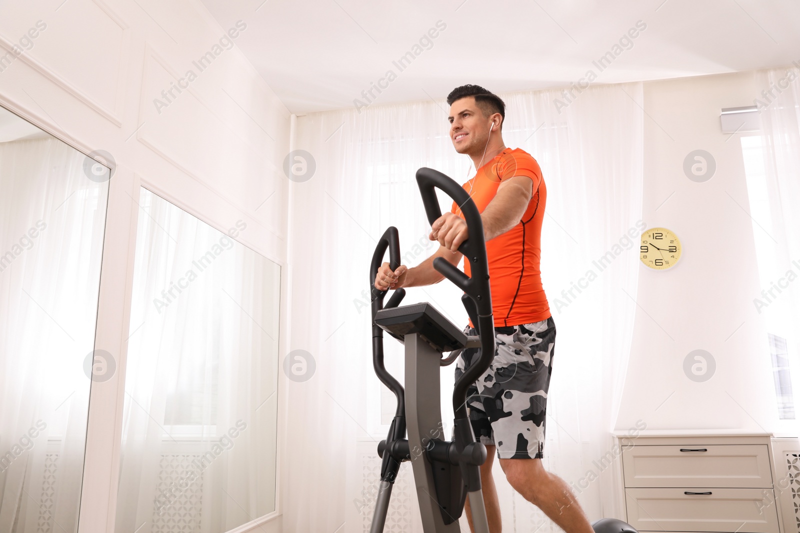 Photo of Man using modern elliptical machine at home