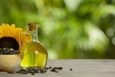 Sunflower cooking oil, seeds and yellow flower on wooden table outdoors, space for text