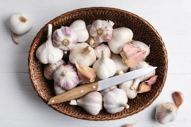 Photo of Fresh organic garlic in wicker basket on white wooden table, flat lay
