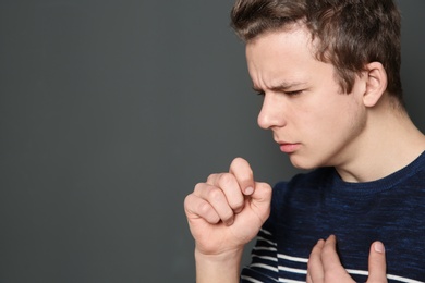 Photo of Teenage boy suffering from cough on dark background. Space for text