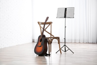 Photo of Acoustic guitar, chair and note stand with music sheets indoors