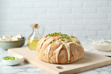 Photo of Freshly baked bread with tofu cheese and green onion on white marble table
