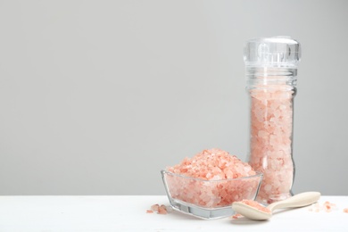 Photo of Pink himalayan salt on white wooden table against grey background. Space for text