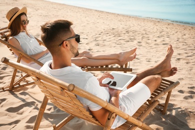 Photo of Young couple relaxing in deck chairs on sandy beach