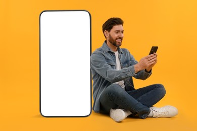 Image of Man with mobile phone sitting near huge device with empty screen on orange background. Mockup for design