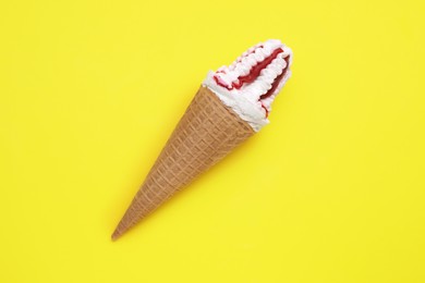 Photo of Delicious ice cream with raspberry jam in waffle cone on yellow background, top view