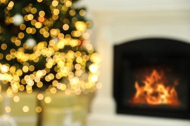 Photo of Blurred view of Christmas tree with bright string lights in room near fireplace. Bokeh effect