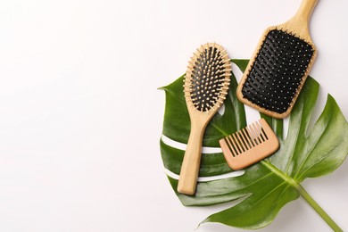 Photo of Wooden hairbrushes, comb and green leaf on white background, flat lay. Space for text