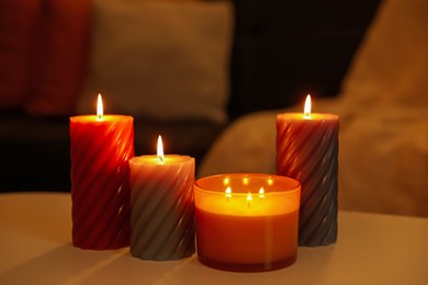 Photo of Burning candles on white table indoors. Cosy atmosphere