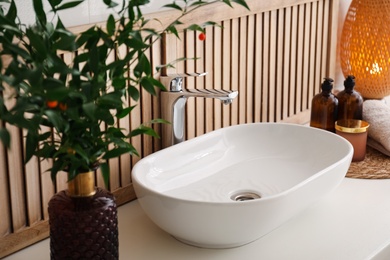 Photo of Vase with beautiful branches and candles near vessel sink in bathroom. Interior design