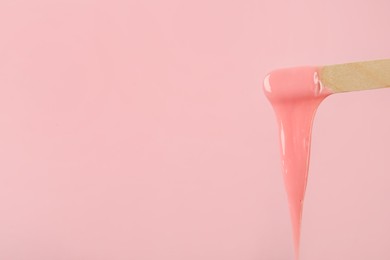 Photo of Wooden spatula with hot depilatory wax on pink background. Space for text