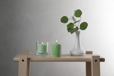 Scented candles near vase with eucalyptus branch on wooden table