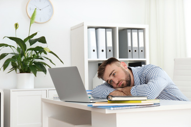 Photo of Lazy young man wasting time at table in office