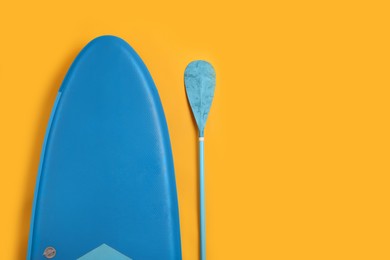 Photo of SUP board and paddle on yellow background, flat lay with space for text. Water sport