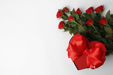 Photo of Heart shaped gift box with bow and beautiful red roses on white background, flat lay. Space for text