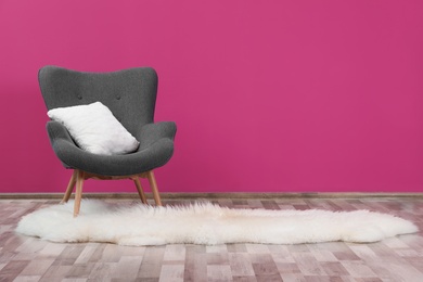 Photo of Comfortable armchair with white cushion and rug against color wall