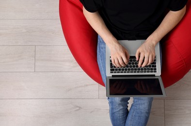 Photo of Man working with laptop in beanbag chair, top view. Space for text