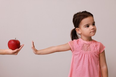 Photo of Cute little girl refusing to eat apple on grey background