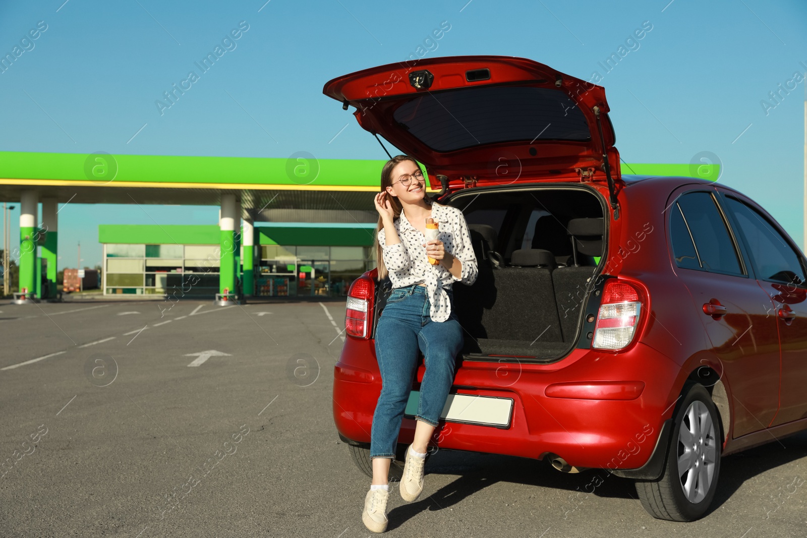 Photo of Beautiful young woman with hot dog near car at gas station