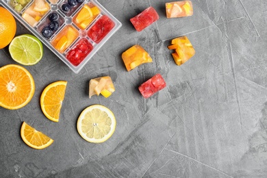 Photo of Flat lay composition with ice cube tray and fresh fruits on grey background. Space for text