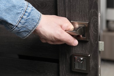 Photo of Man opening wooden door indoors, closeup of hand on handle