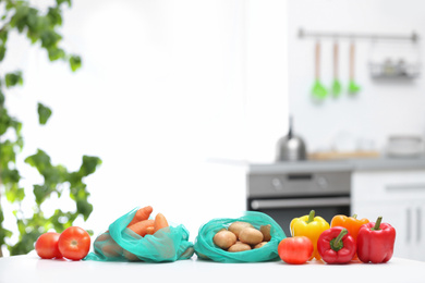 Photo of Net bags with vegetables on wooden table in kitchen