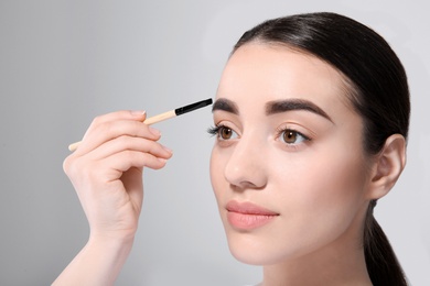 Photo of Beautiful woman with perfect eyebrows applying makeup on light background