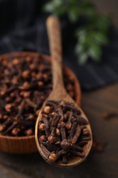 Photo of Bowl and spoon with aromatic cloves on wooden table, closeup