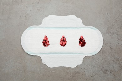 Menstrual pad with drops made of red sequins on grey background, top view