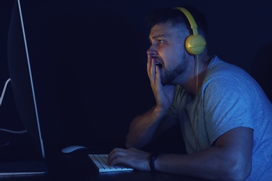 Photo of Upset man with headphones playing video game on modern computer at dark room