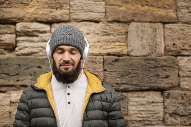 Photo of Mature man with headphones listening to music near stone wall. Space for text