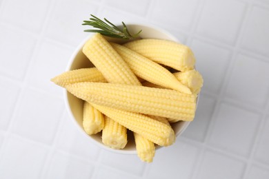 Photo of Tasty fresh yellow baby corns in bowl on white tiled table, top view