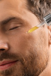 Photo of Handsome man applying cosmetic serum onto his face, closeup