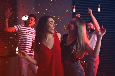 Photo of Happy friends and falling confetti in dark room