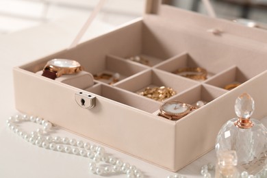 Photo of Jewelry box with many different accessories and perfume on white table, closeup