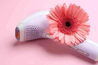 Photo of Modern photoepilator and flower on pink background, closeup