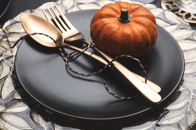 Photo of Autumn table setting with golden cutlery and pumpkin on black background, closeup