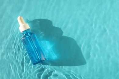 Photo of Bottle of cosmetic serum in water on turquoise background, top view. Space for text