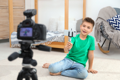 Photo of Cute little blogger with phone and selfie stick recording video at home