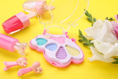 Photo of Decorative cosmetics for kids. Eye shadow palette, lipsticks, accessories and flowers on yellow background, closeup