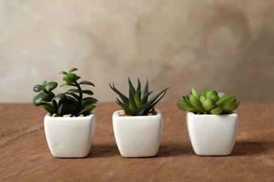 Photo of Beautiful artificial plants in flower pots on brown table