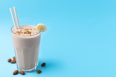 Photo of Glass of tasty banana smoothie with straws and almond on light blue background. Space for text