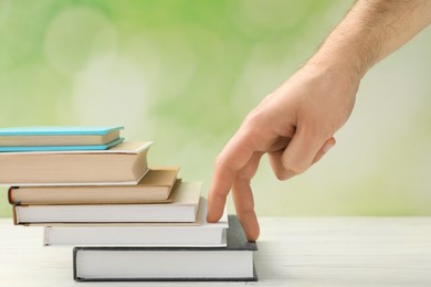 Photo of Man climbing up stairs of books with fingers on white wooden table against blurred background, closeup