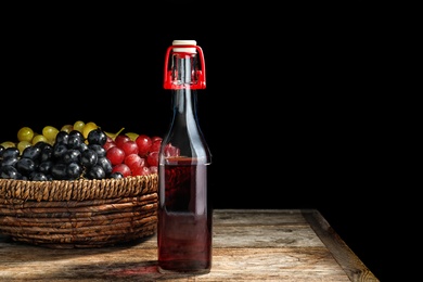 Photo of Bottle of wine vinegar and basket with fresh grapes on wooden table against black background. Space for text