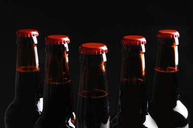 Photo of Bottles of tasty cold beer on black background, closeup