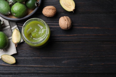 Photo of Feijoa jam and fresh fruits on black wooden table, flat lay. Space for text