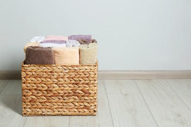 Photo of Wicker laundry basket with clean terry towels on floor indoors, space for text